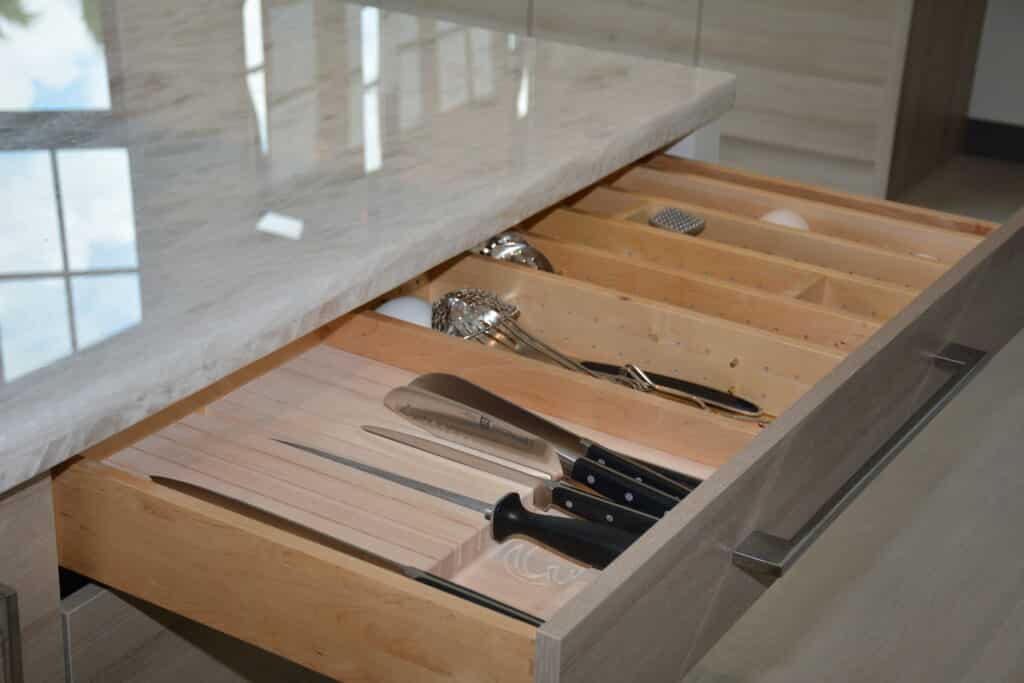 Open kitchen drawer with organized wooden dividers holding knives, utensils, and a peeler.