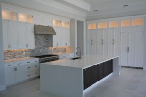 Modern kitchen with white laminate cabinets, a large dark island, stainless steel appliances, stone backsplash, and bright under-cabinet lighting.