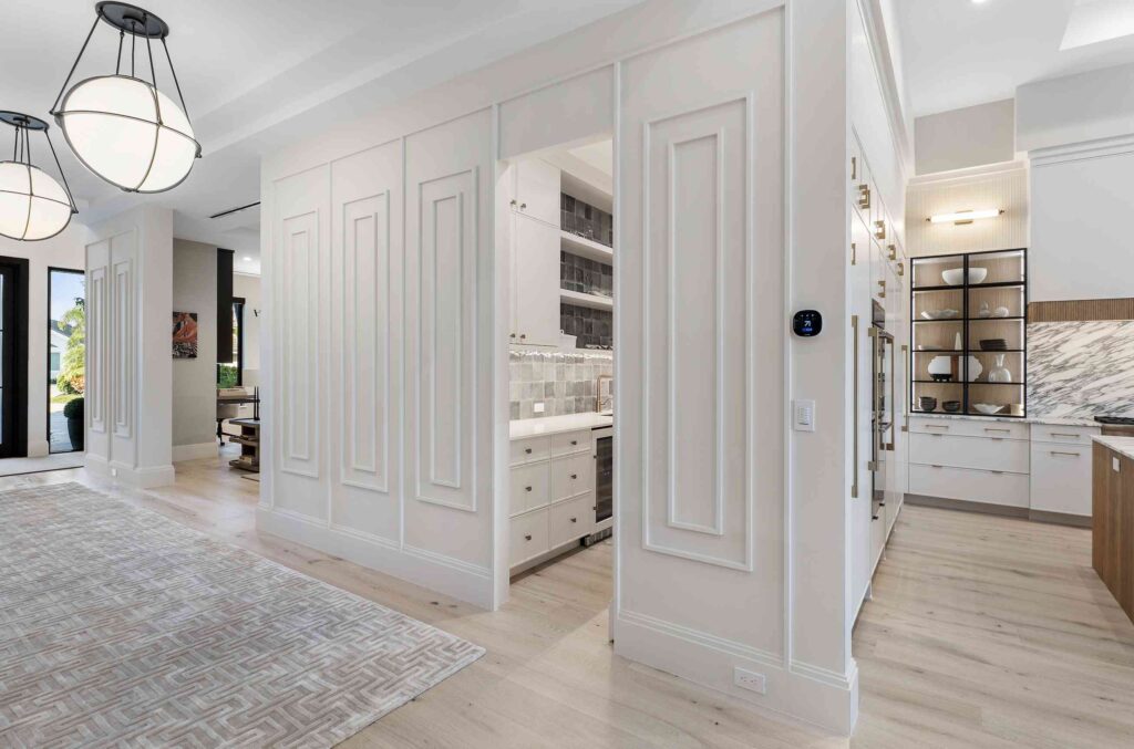 Spacious modern kitchen featuring high-end cabinetry with white cabinets, recessed lighting, and a view into the dining area. Light wood flooring and geometric-patterned carpet enhance the clean, open layout.